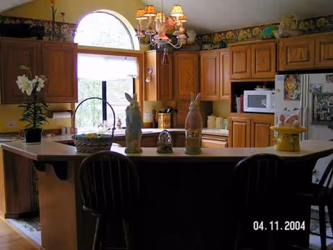 A warm kitchen with wooden cabinets, island, and decorative figurines in a senior living setting.