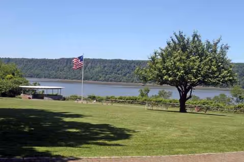 Lush lawn with flag, tree, picnic tables, and a lake beyond.