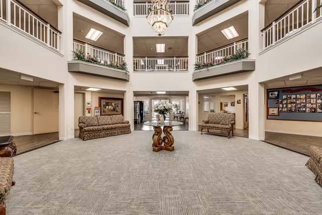 Spacious two-story atrium lobby with seating, a central table of flowers, surrounding balconies, and a hanging chandelier.