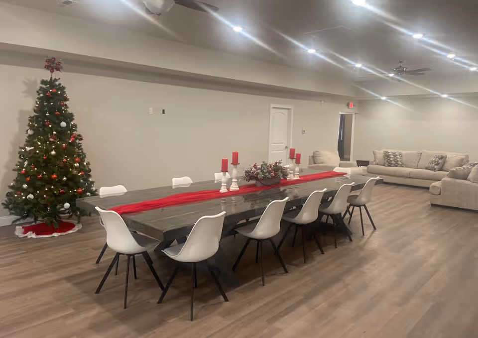 Spacious communal dining and lounge area with a long table and chairs, sofas, and a decorated Christmas tree.