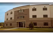 Exterior view of a three-story beige senior living facility with an entrance.