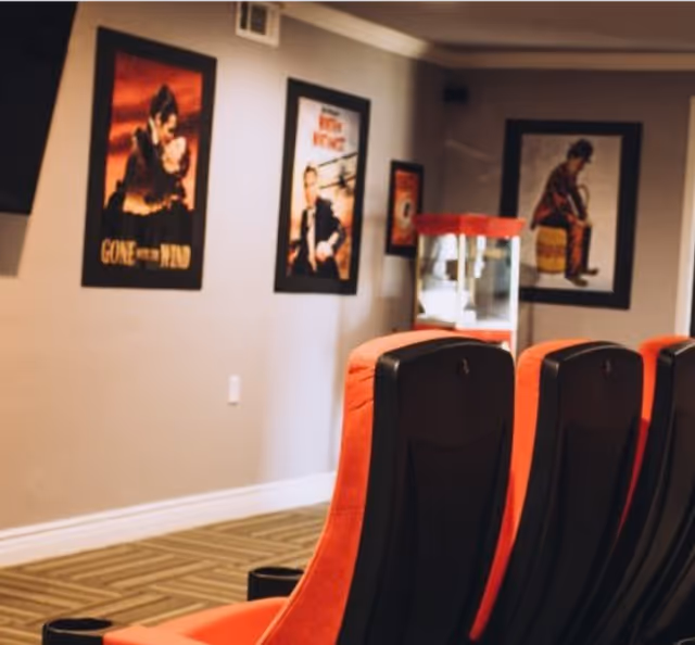 Rows of red theater-style seats facing a wall decorated with framed movie posters and a popcorn machine.