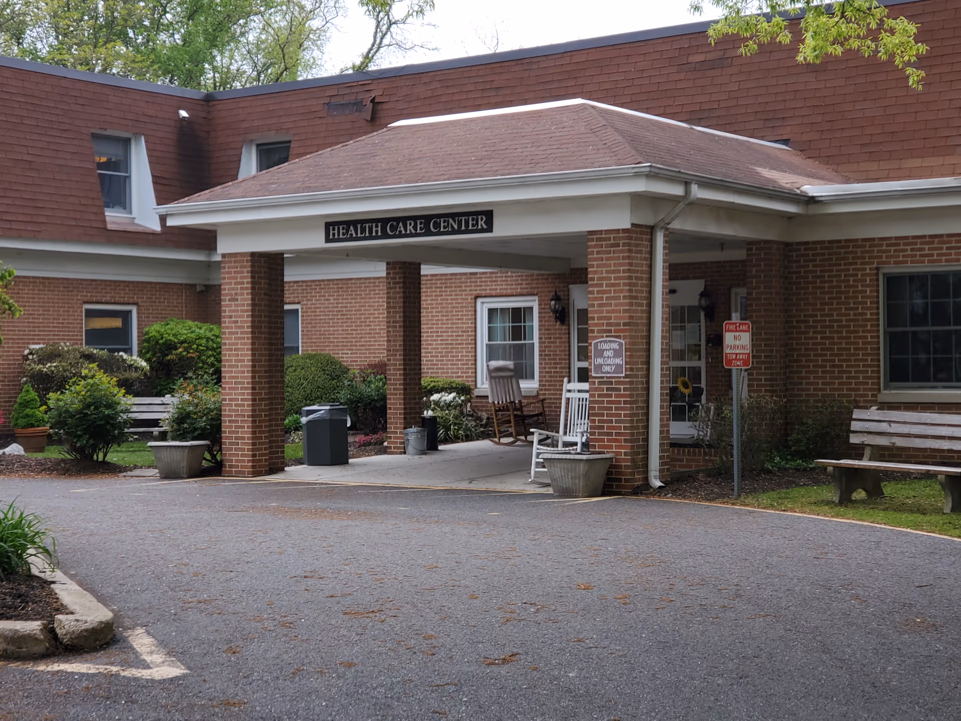 Front entrance canopy of a health care center with rocking chairs, benches, planters and a driveway.