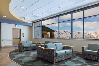 Bright sitting lounge with clustered upholstered armchairs and sofas around a patterned circular rug beneath large windows showing a mountain view.