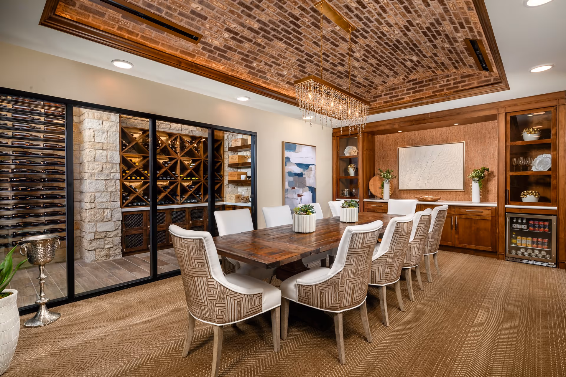 Elegant dining room with a long wooden table, upholstered chairs, a crystal chandelier, and a glass-enclosed wine cellar.