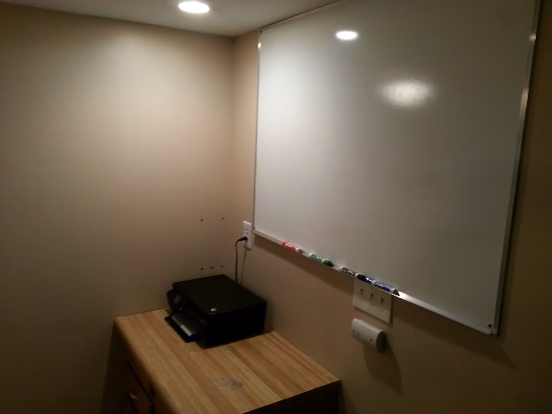 Small interior office nook with a wall-mounted whiteboard, markers, and a desk holding a printer.
