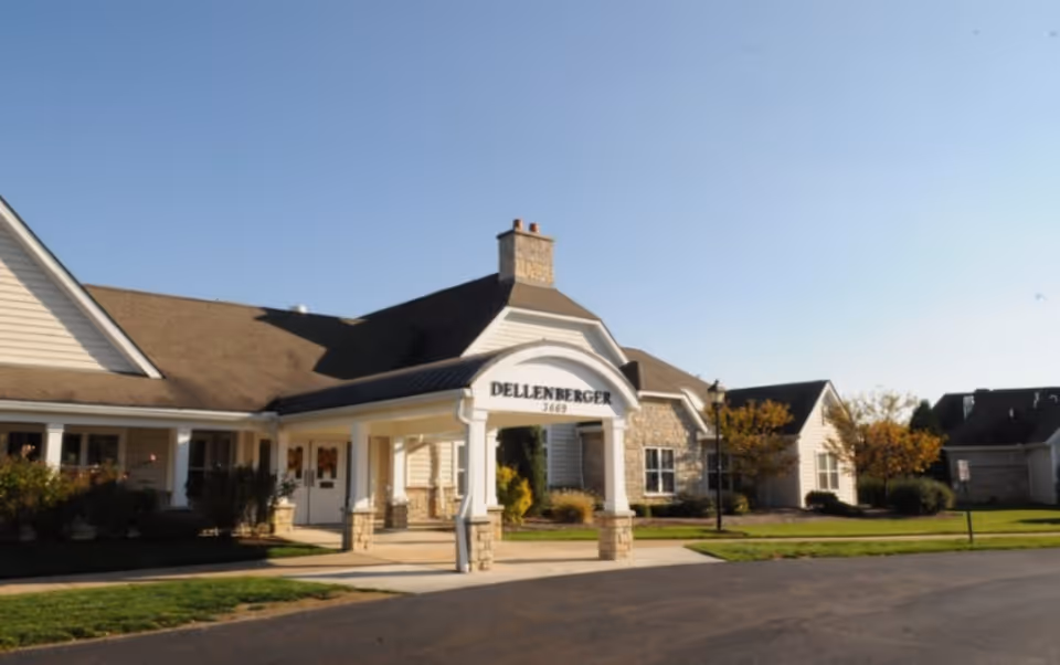 Front entrance of a single-story senior living building with a covered porte-cochère labeled 'Dellenberger' and surrounding landscaping.