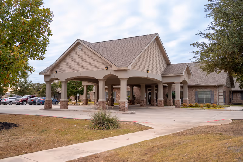 Front entrance of The Heights on Huebner, a senior living community, featuring a covered porte-cochère and parked cars.