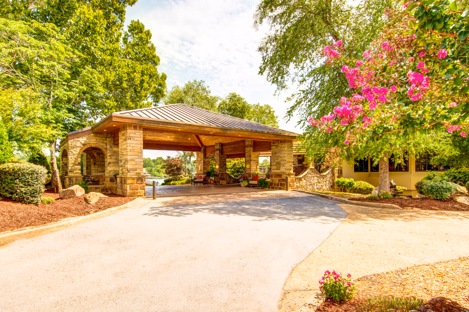 Covered stone porte-cochere entrance with landscaped grounds and flowering trees.