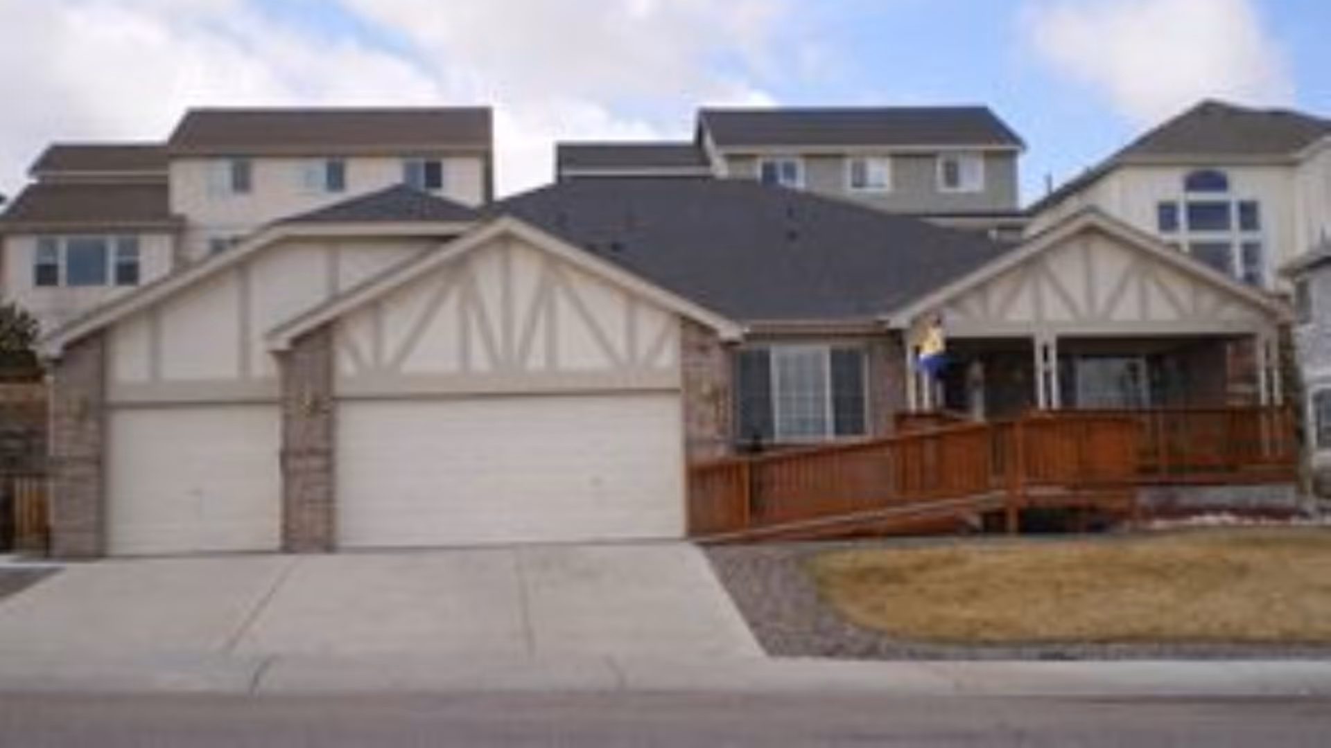 Exterior view of a senior living facility with a two-car garage, beige siding, and a deck.