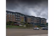 A large brick senior living facility along a street with parked cars and a cloudy sky.