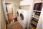 Laundry room with front-loading washer and dryer, shelving, a hanging rod, and a view into a hallway.