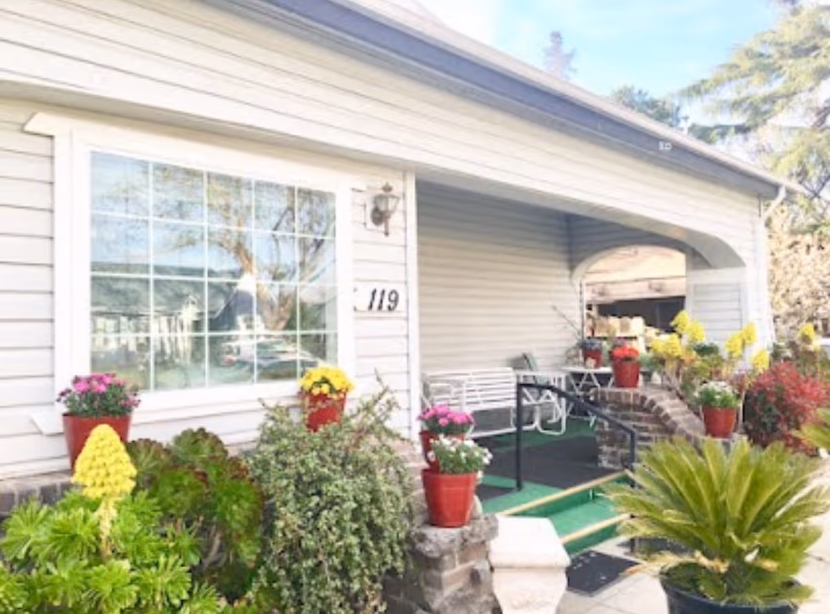 Front entrance and covered porch of a single-story home with potted flowers, a bench, a ramp, and house number "119".