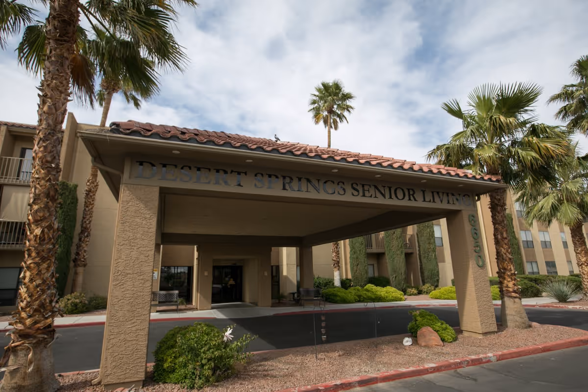 Entrance to Desert Springs Senior Living facility with a covered drop-off area, palm trees, and landscaping around the driveway.