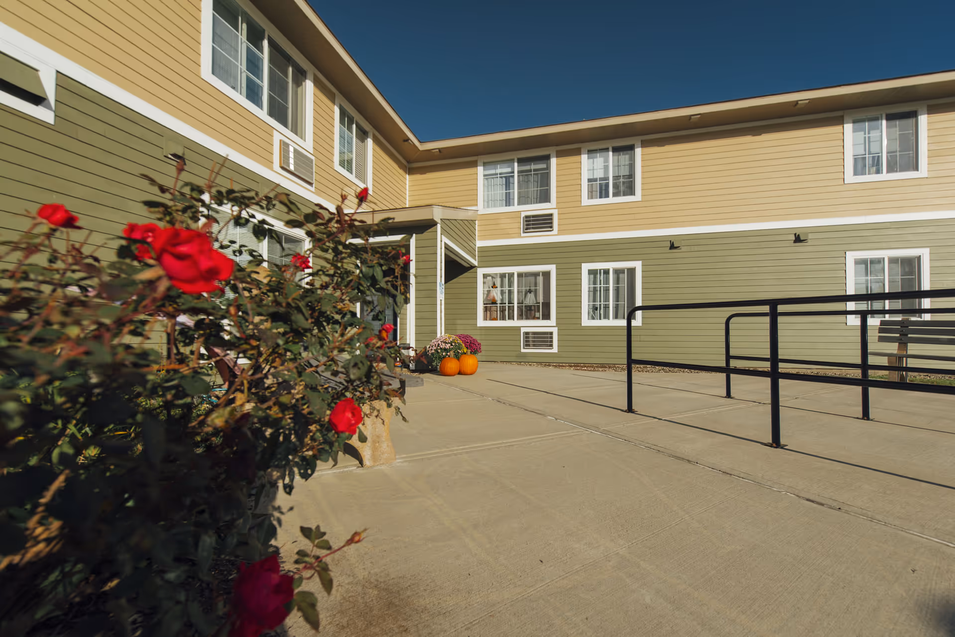 Exterior view of Branson Manor Senior Apartments showing the entrance, walkway, ramp, and rose bushes.