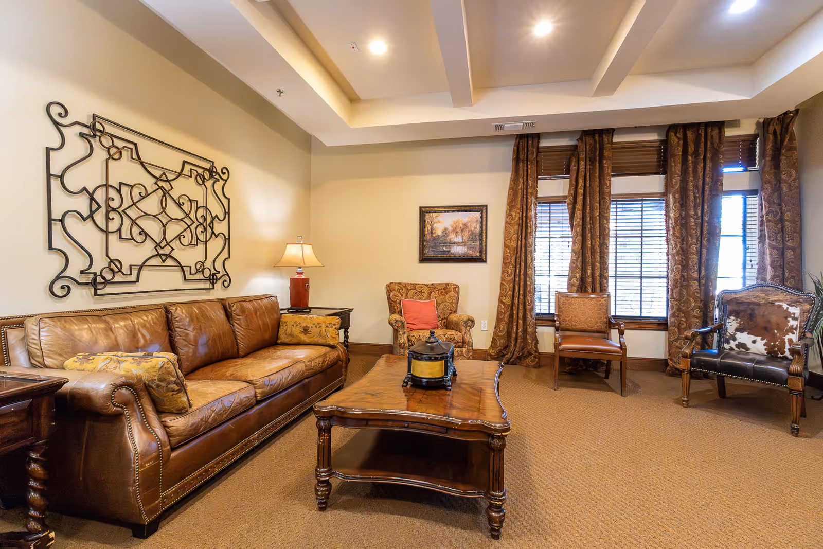 A warm living room with a brown leather sofa, armchairs, a wooden coffee table, decorative wall art, and windows with drapes.