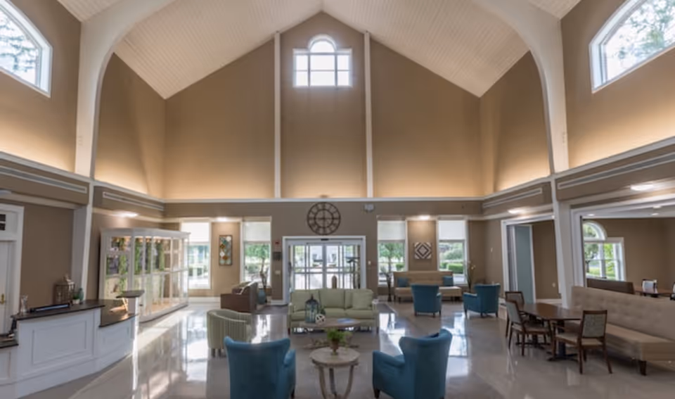 Spacious senior living community lobby with vaulted ceilings, multiple seating areas, and a reception desk.