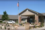 Exterior view of Bethany Home Sioux Falls facility entrance with a covered drop-off area, stone landscaping, small trees, and an American flag on a flagpole.