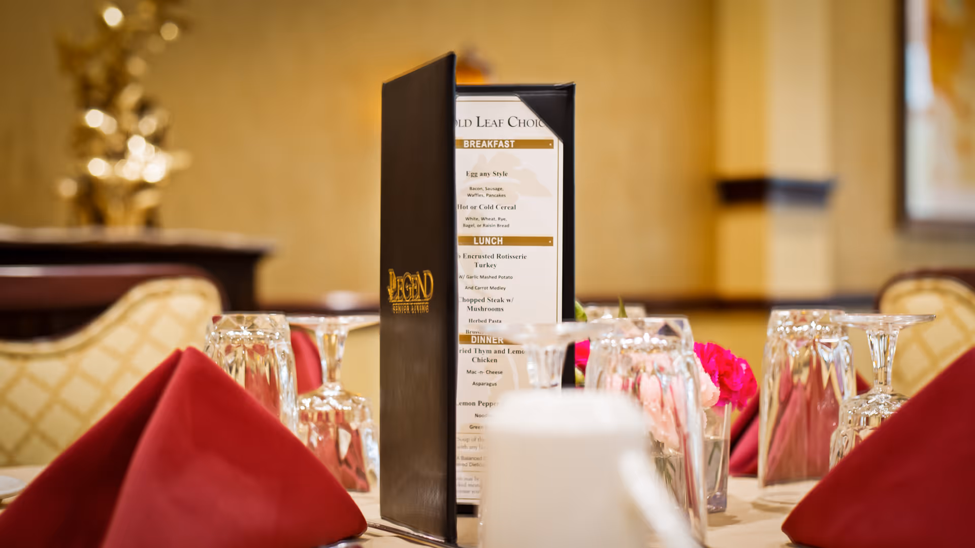 Table set for a meal with folded red napkins, glassware, flowers, and a standing menu bearing the 'Legend' logo in a dining room.