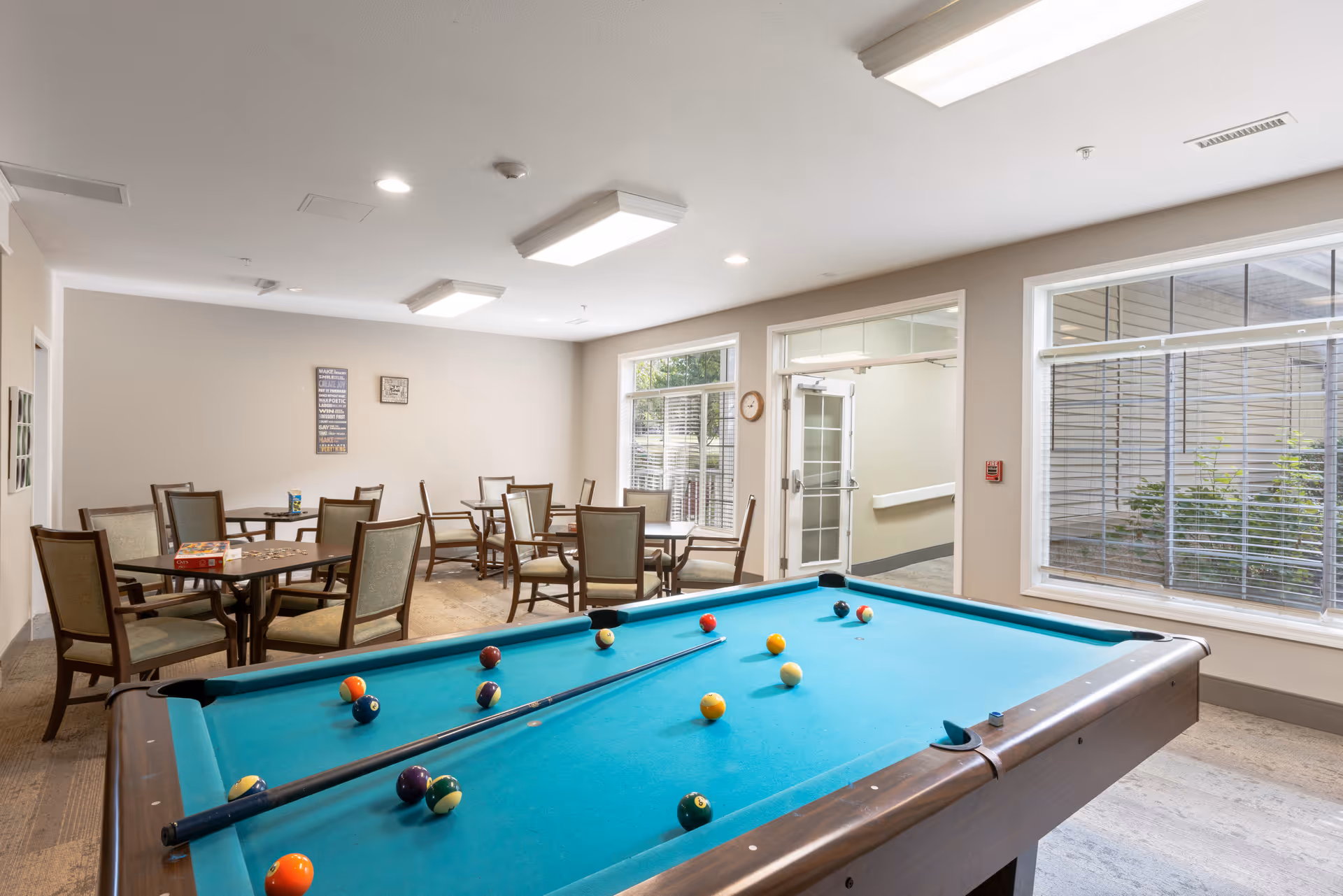 Community game room with a pool table in the foreground and several tables and chairs in the background.