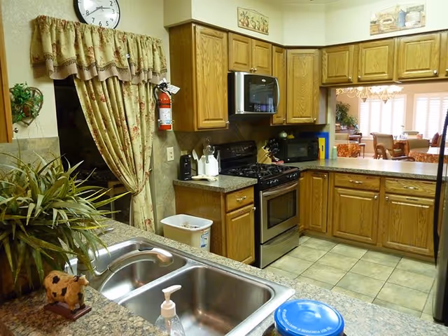 Interior view of a kitchen with oak cabinets, stainless steel stove and microwave, a double sink in the foreground, and a pass-through to a dining area.