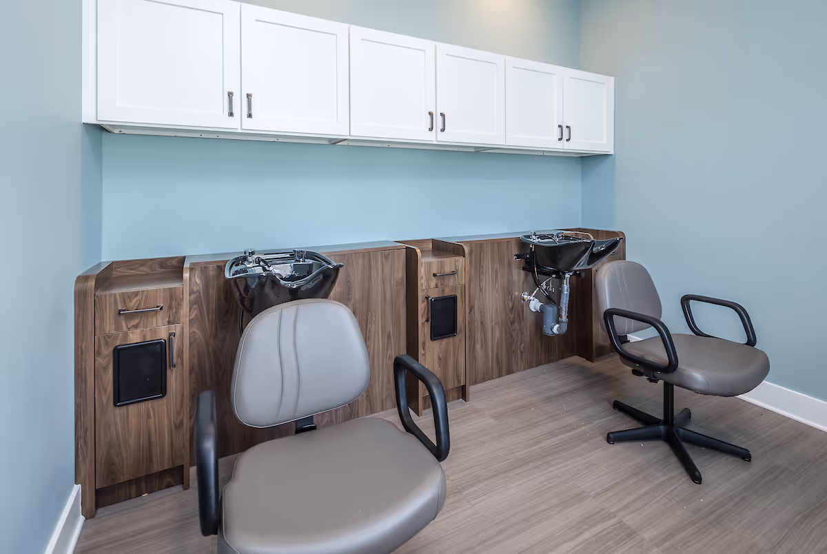 A small salon area with two styling chairs, two black shampoo sinks, wood cabinetry and white wall cabinets against blue-green walls.