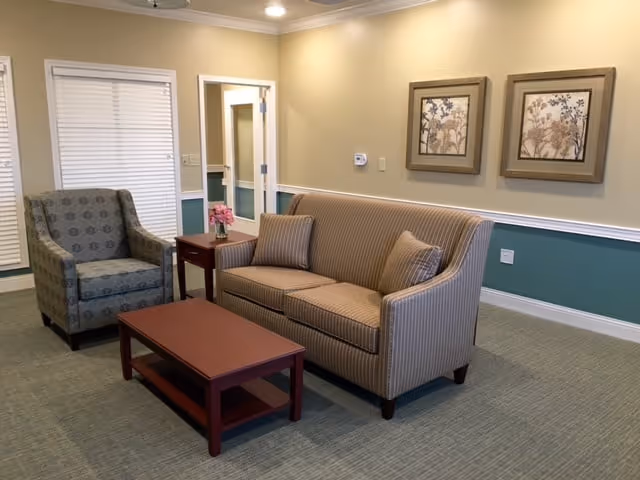 A communal lounge with a striped sofa, patterned armchair, coffee table and side table against a beige and green wall.