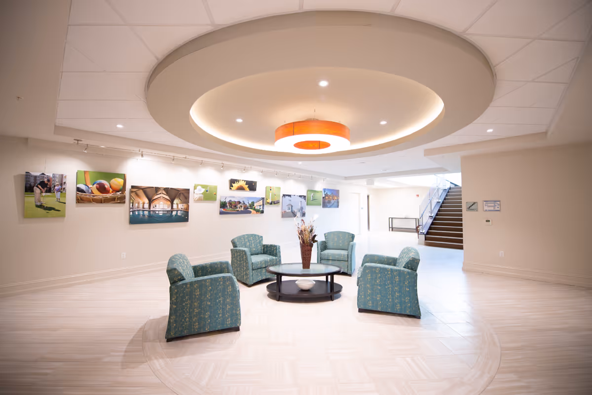 Bright lobby lounge with a circular ceiling light, four upholstered chairs around a coffee table and artwork on the wall.