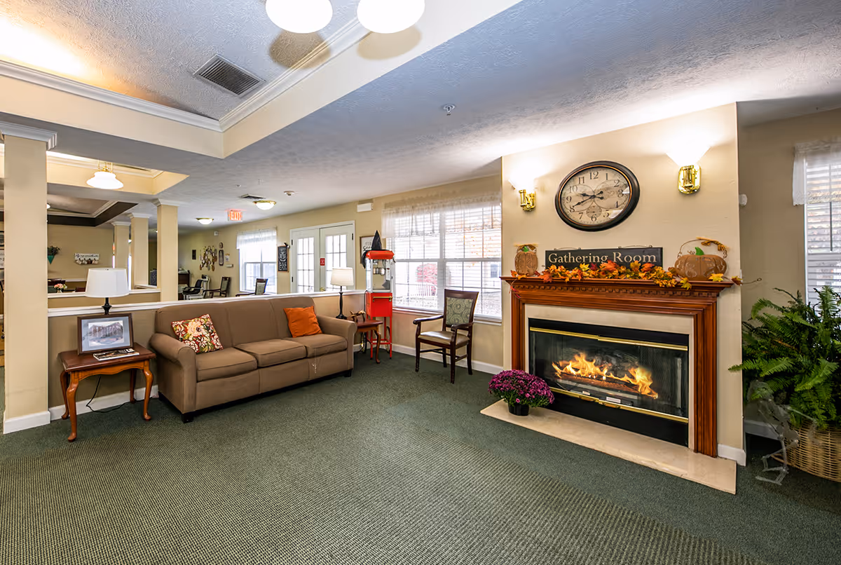 A cozy gathering room with a sofa, chairs, a decorative fireplace labeled 'Gathering Room', and large windows.