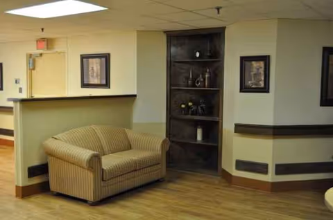 Lobby seating area with sofa, reception desk, and display shelf in a senior living facility.