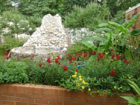 Colorful garden with a stone fountain and brick planter.