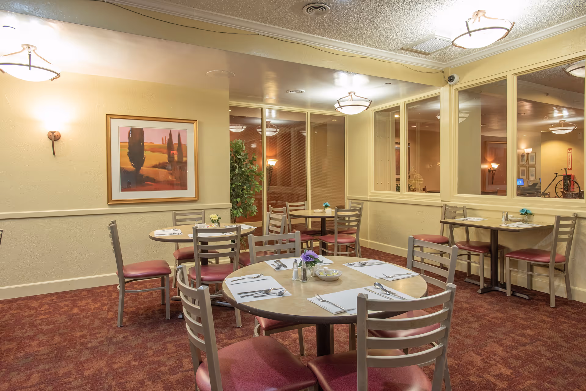 Small dining room with round tables set for meals, chairs, artwork on the wall, and warm lighting.