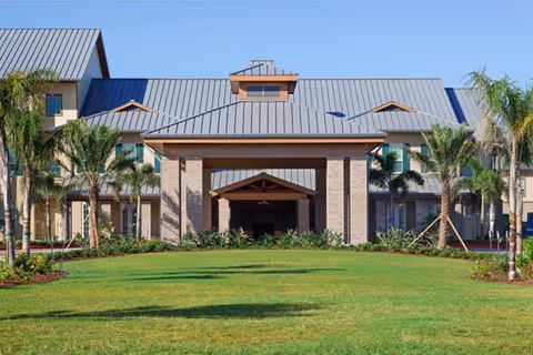 Front view of Mirador Retirement Community building with lawn and palm trees.