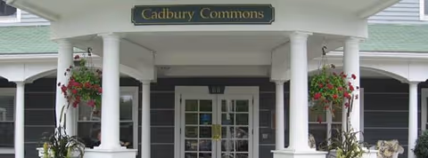 Covered entrance to Cadbury Commons with white columns, hanging flower baskets, and glass double doors.