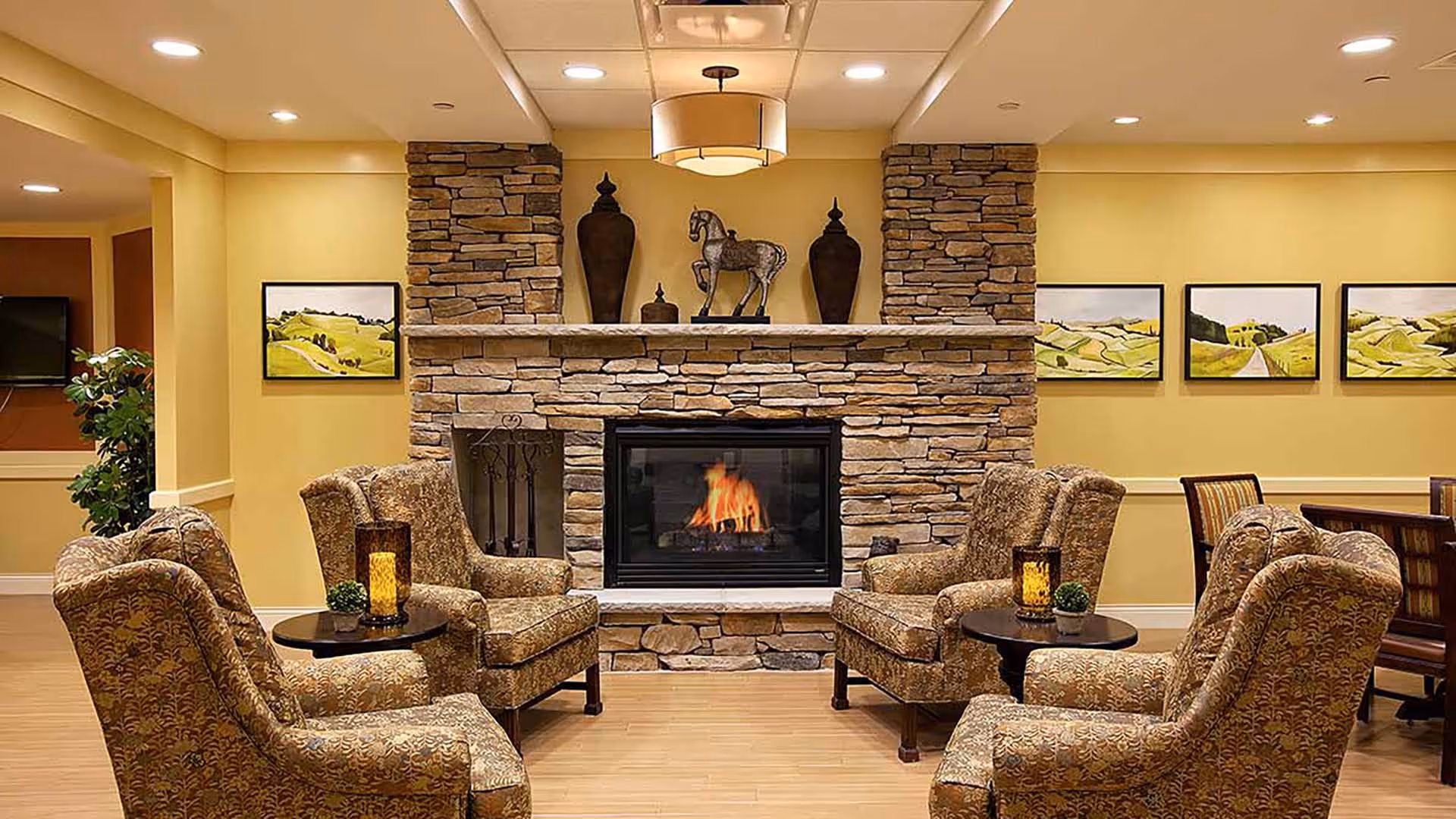 Cozy communal lounge with a stone fireplace flanked by upholstered armchairs and small tables under warm lighting.