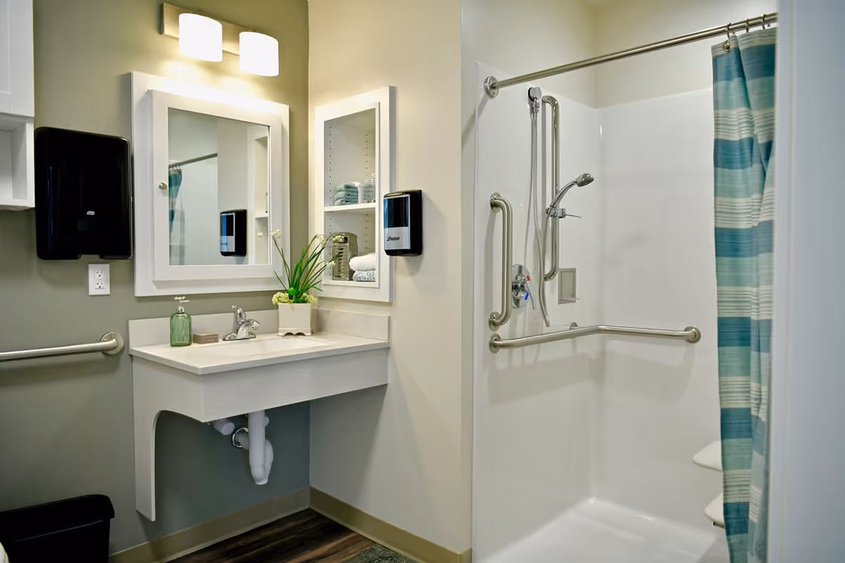 Accessible bathroom with a vanity and mirror on the left and a shower with grab bars and a striped curtain on the right.