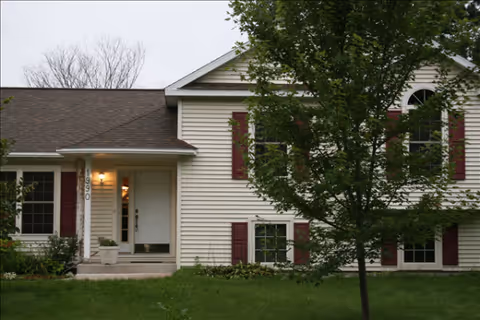 Exterior view of a beige two-story building with maroon shutters and a front entrance.