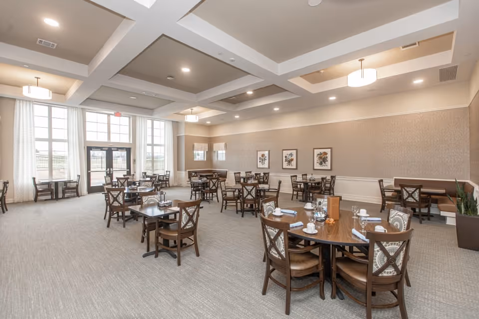 Large, bright dining room with multiple set tables, high coffered ceilings and tall windows.