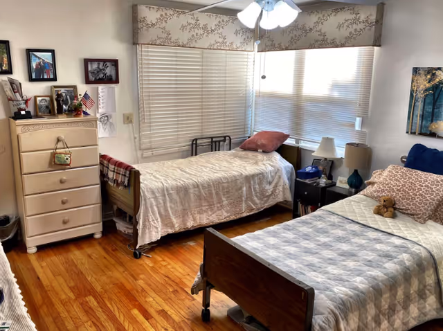 Sunny bedroom with two single beds, a dresser, bedside tables and window blinds.