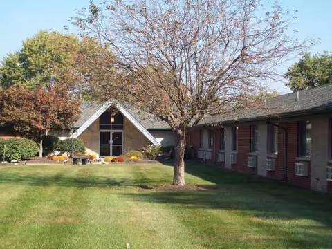 Exterior view of a single-story brick senior living facility with a lawn and trees.
