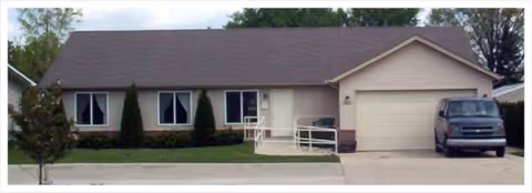 Single story beige senior facility exterior with front entrance, ramp, and a parked vehicle