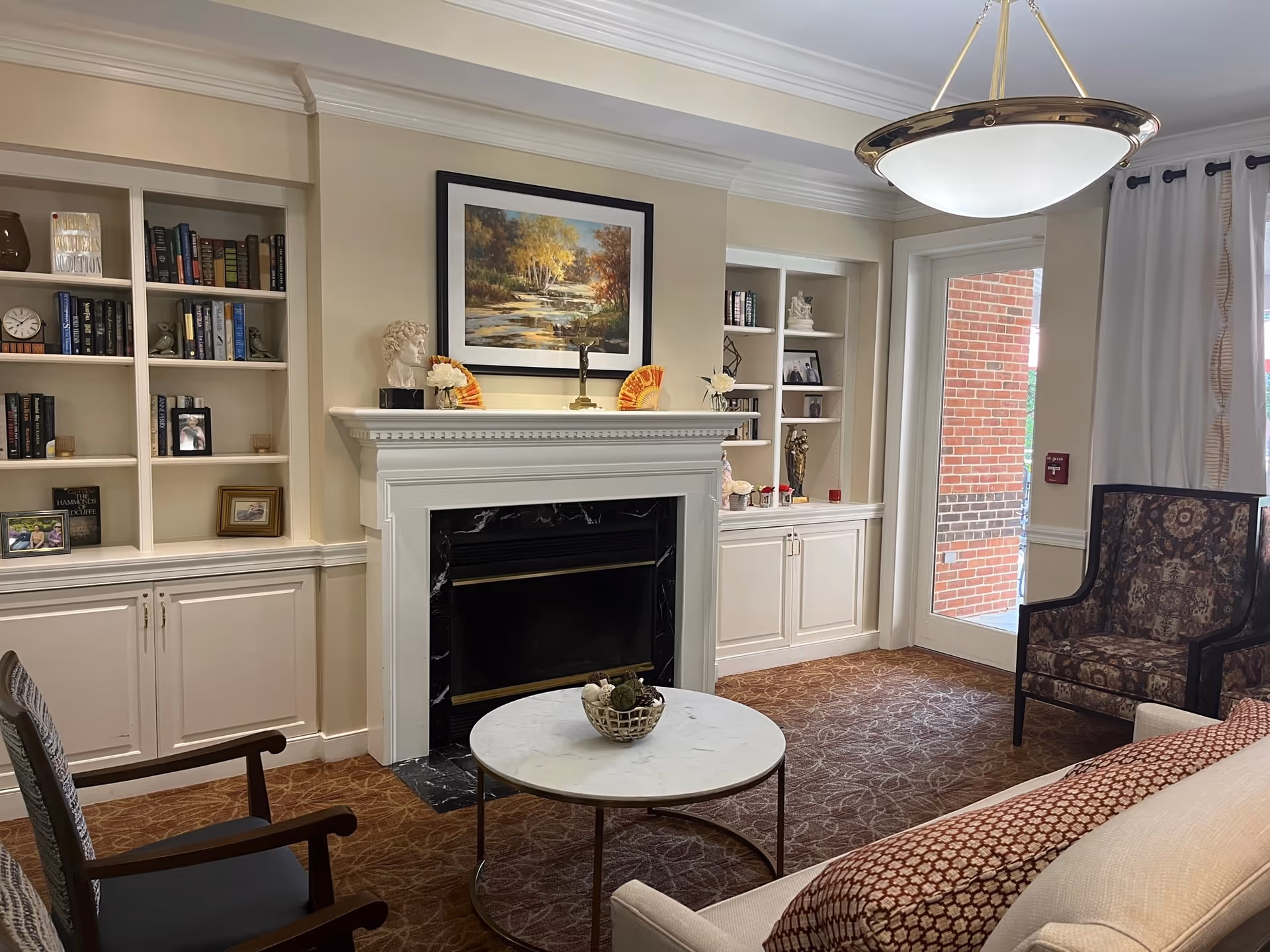 Cozy common living room with a fireplace, built-in bookshelves, seating, and a round marble coffee table.