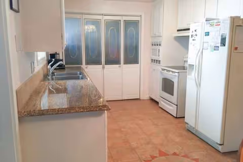 Bright kitchen in Lucia's Adult Family Home with granite countertops, white cabinets, fridge, stove, frosted doors.