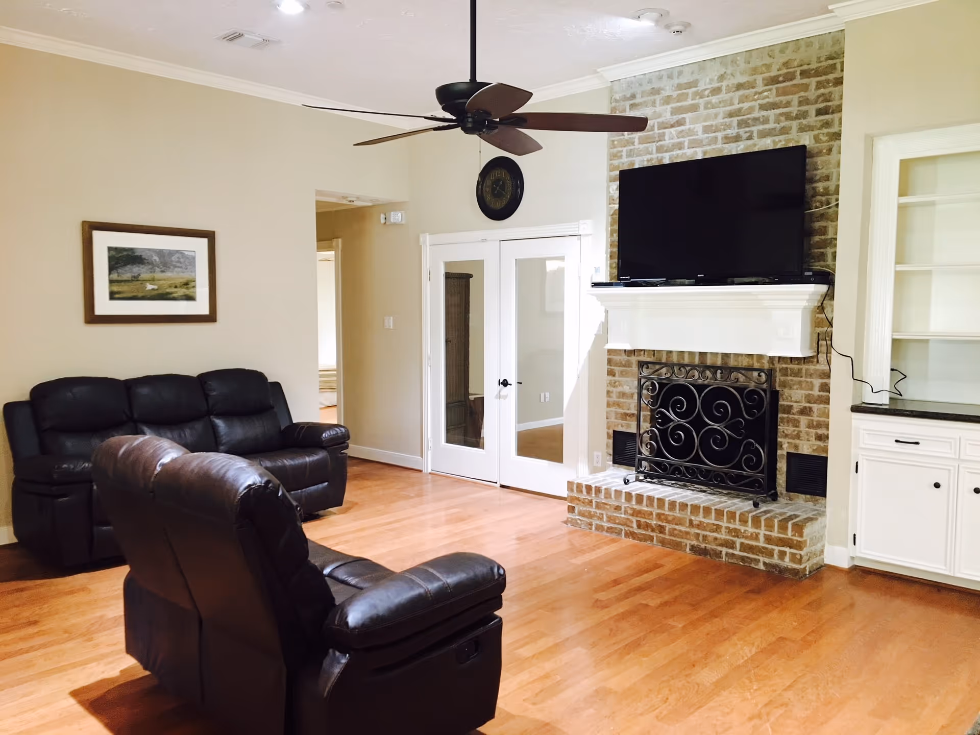Spacious living room with leather recliners, a brick fireplace with a mounted TV, hardwood floors, and a ceiling fan.