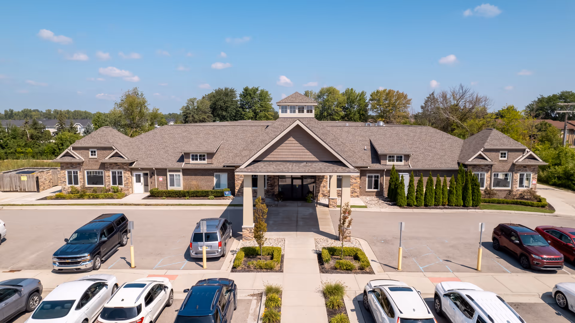 Front exterior of a single-story senior living facility with a covered entrance and cars parked in the lot.