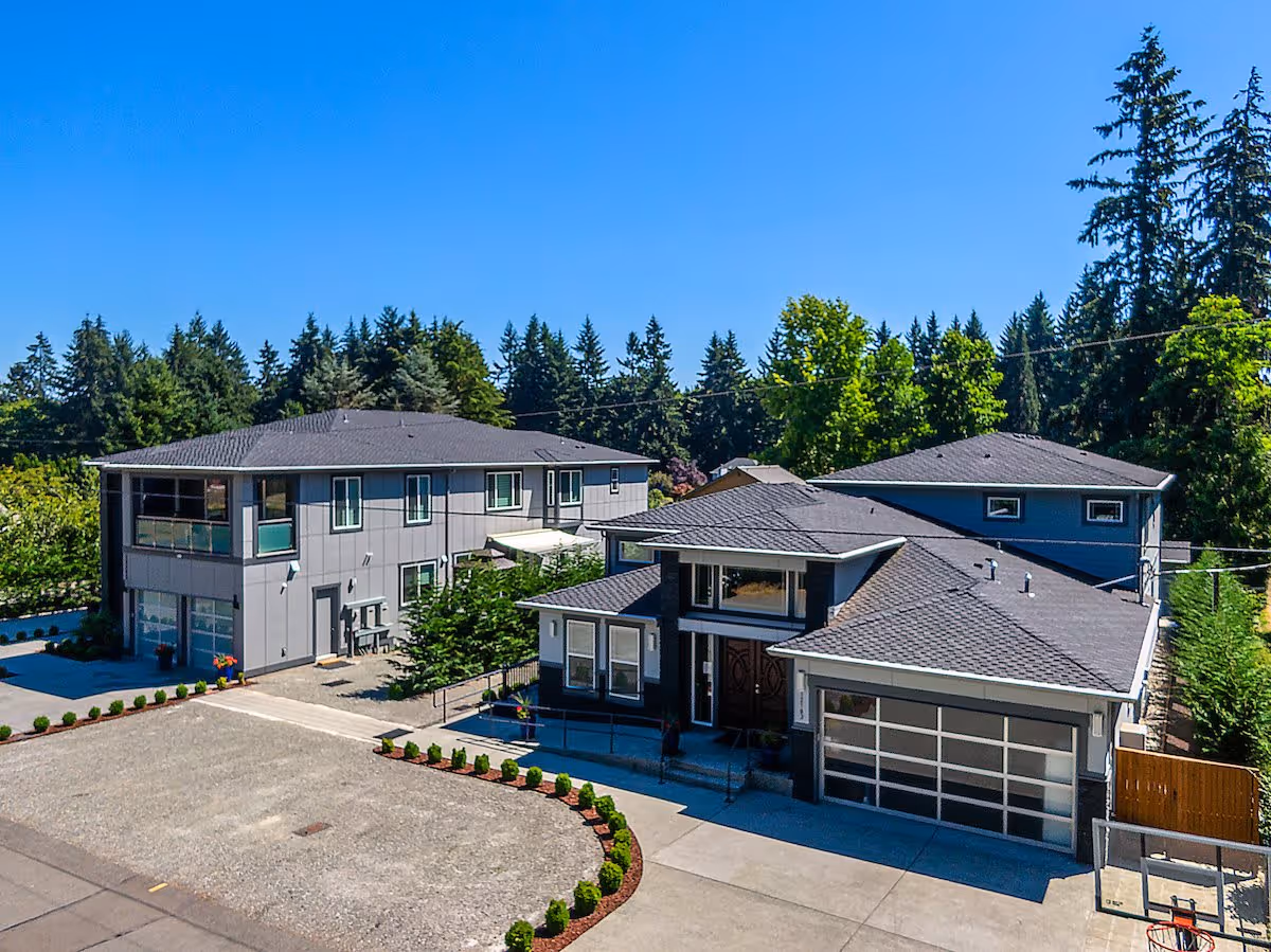 Exterior view of a modern two-building residential facility with gray siding and dark roofs, surrounded by trees and clear blue sky.