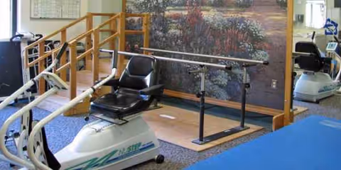Rehabilitation gym with parallel bars, exercise bike, and therapy equipment inside Riverside Nursing and Rehab.