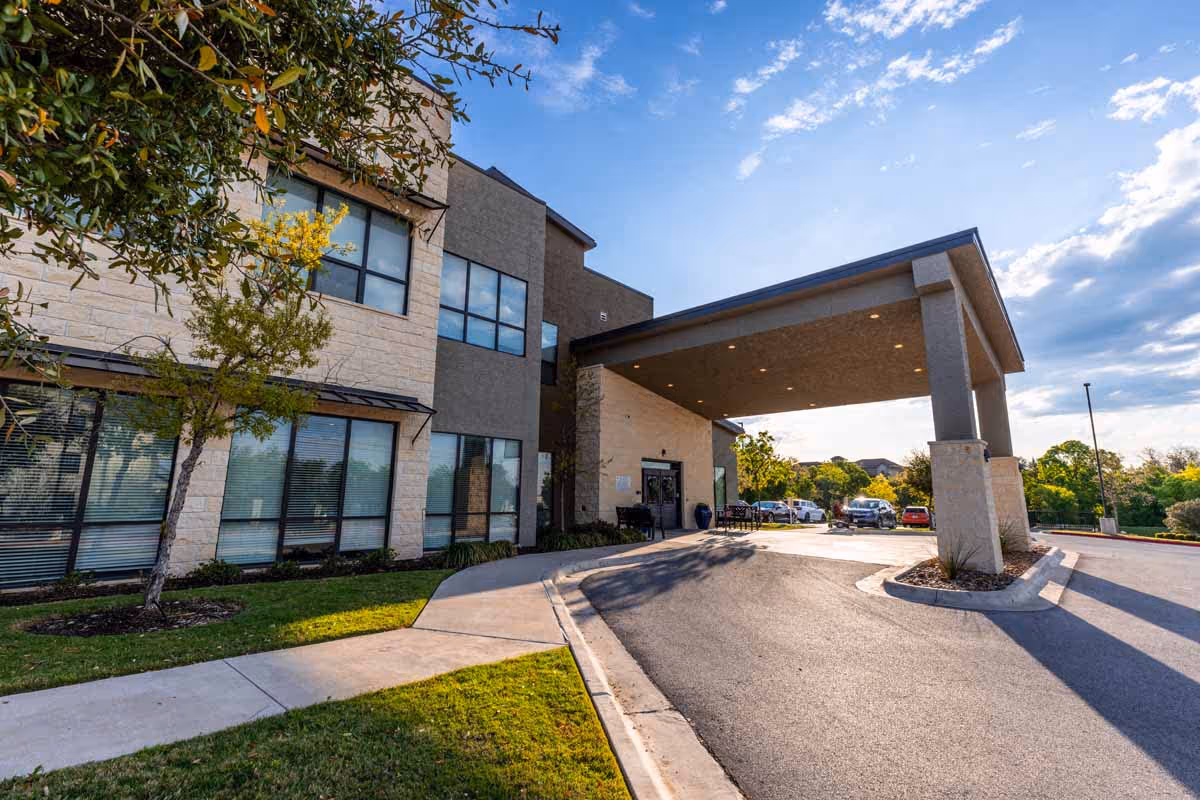Front entrance of Tech Ridge Oaks with a covered porte-cochère, driveway, parked cars, and landscaped lawn under a blue sky.