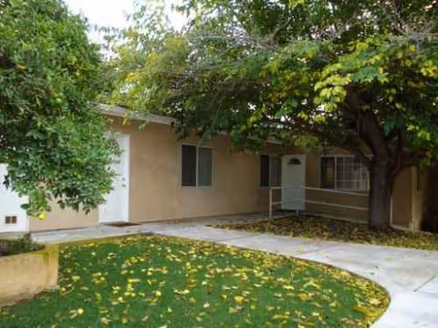 Exterior view of Peppertree Guest Home II with doorway, trees, and fallen leaves.