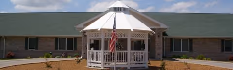 Front exterior of The Manor at Mason Woods with a white gazebo and American flag.